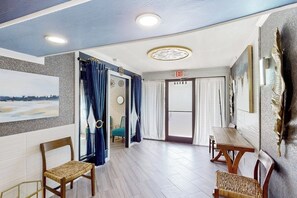 A hotel room with a wooden floor, a dining table, two chairs, a large painting, and an exit door. - The Waves: unit A - Beach Duplex, Full Kitchen (South Padre Island)