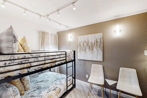 Kerrossänky, jossa on kukkakuviollinen vuodevaatteisto, seinällä oleva taulu ja kaksi valkoista tuolia.