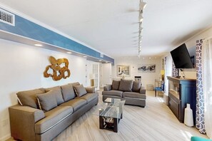 A modern living room with two sofas, a coffee table, a TV, and a decorative wall piece. - The Waves: unit A - Beach Duplex, Full Kitchen (South Padre Island)