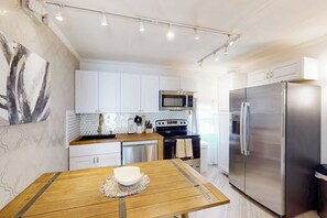A modern kitchen with white cabinets, stainless steel appliances, and a wooden dining table. - The Waves: unit A - Beach Duplex, Full Kitchen (South Padre Island)