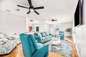 A modern living room with a teal sofa, a coffee table, and a ceiling fan. - Redicare Resort - Upstairs (Galveston)