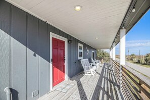 A covered porch with a red door, white railings, and a welcome mat. - Redicare Resort - Upstairs (Galveston)