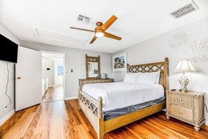 A bedroom with a wooden bed, a ceiling fan, a nightstand, and a door leading to another room. - Redicare Resort - Upstairs (Galveston)