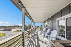 A covered porch with white Adirondack chairs and a view of a body of water and buildings in the distance. - Redicare Resort - Upstairs (Galveston)