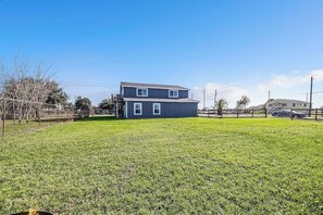 A two-story house with a fenced yard and a clear sky. - Redicare Resort - Upstairs (Galveston)