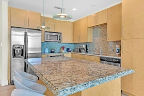 A modern kitchen with granite countertops, stainless steel appliances, and wooden cabinets. - Sapphire Condominiums #806 (South Padre Island)