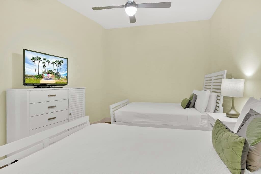 A hotel room with a bed, a TV, a ceiling fan, and a nightstand with a lamp.