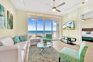 A living room with a sofa, armchair, coffee table, and a TV. There is a balcony with a view of the ocean. - Sapphire Condominiums #806 (South Padre Island)
