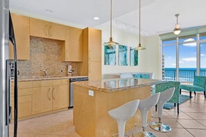 A modern kitchen with granite countertops, stainless steel appliances, and a central island with bar stools. - Sapphire Condominiums #806 (South Padre Island)
