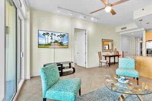 A spacious living room with a ceiling fan, a television mounted on the wall, and a dining area with a table and chairs. - Sapphire Condominiums #806 (South Padre Island)