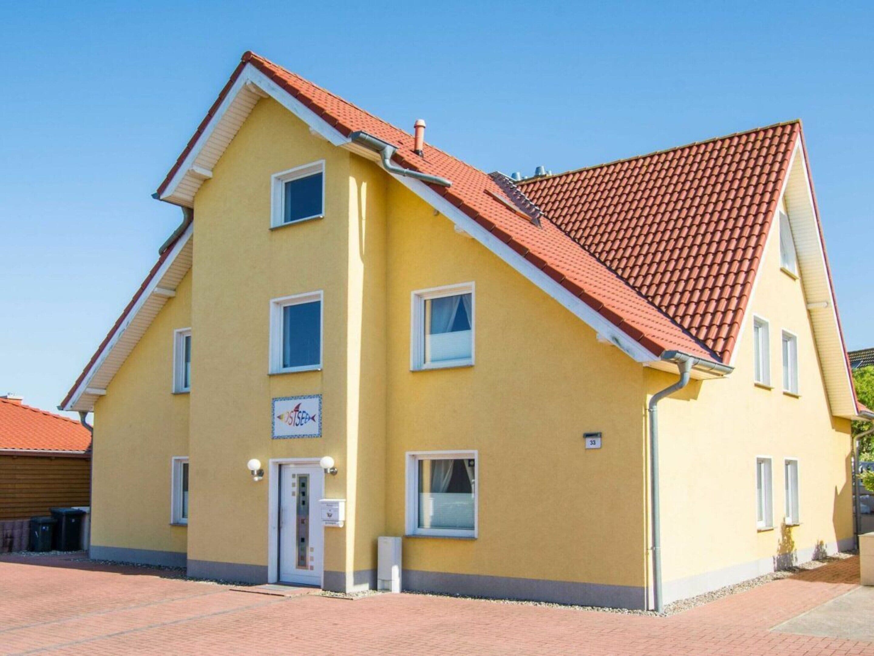 A yellow building with a red-tiled roof, a door, and a sign indicating a business or service.
