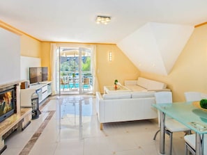 A modern living room with a fireplace, a television, a glass coffee table, a sofa, and a dining area with chairs. - Holiday Apartment With 1 Bedroom (Heringsdorf)