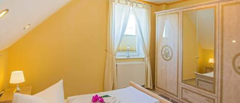 A hotel room with a bed, a nightstand, a lamp, a wardrobe, and a window with curtains.