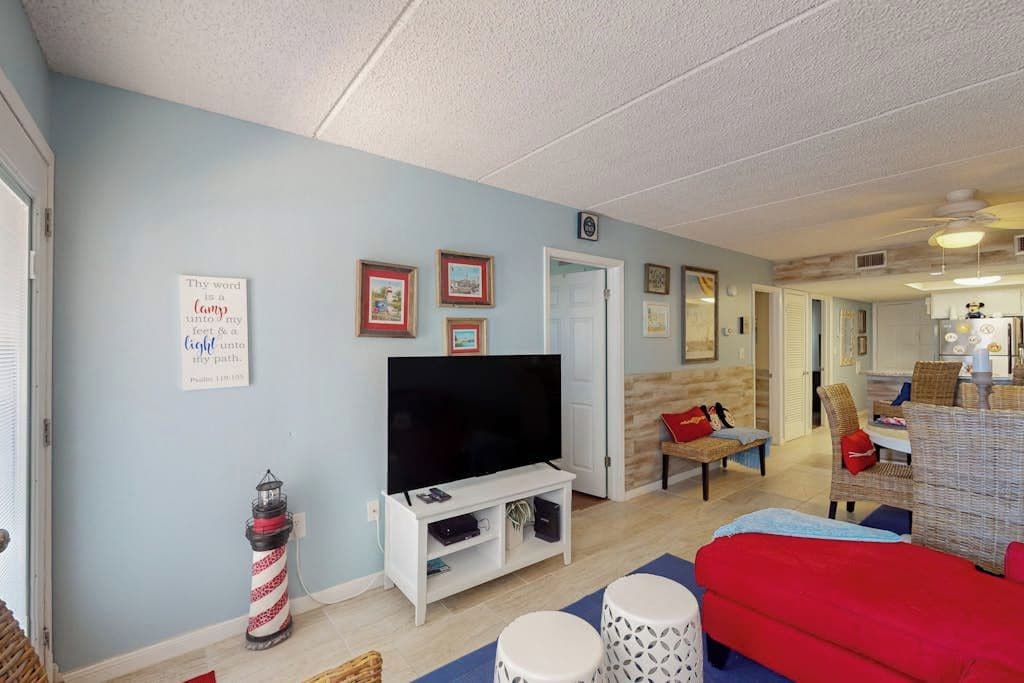 A living room with a television, a red sofa, a small table, and a wall-mounted shelf.