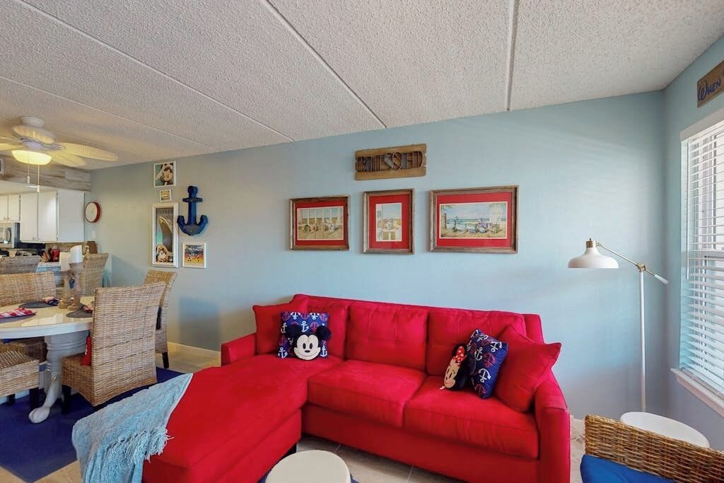 Una habitación con un sofá rojo, muebles de mimbre, cuadros enmarcados y un ventilador de techo.