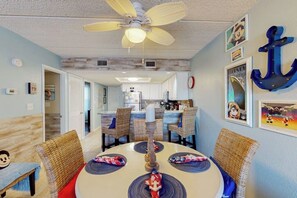 A dining area with a round table, wicker chairs, and a ceiling fan. - Surfside II Unit 309 (South Padre Island)