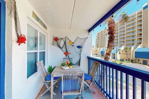 A balcony with a table, chairs, and a view of a hotel building. - Surfside II Unit 309 (South Padre Island)