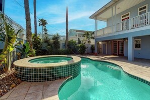 Una piscina amb una banyera d'hidromassatge, envoltada de palmeres i un edifici de dues plantes amb un balcó.
