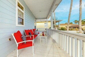 A covered porch with white railings, red and white outdoor furniture, and a view of palm trees and buildings in the background. - Lantana Oasis - Private Pool, Hot Tub & Dogs OK (South Padre Island)