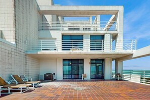 Ein modernes Gebäude mit einer Terrasse, Sitzmöglichkeiten im Freien und Blick auf das Meer.