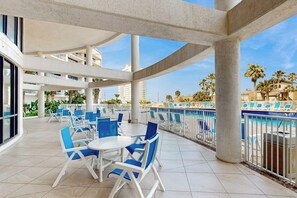 An outdoor terrace with a pool, blue chairs, and a white table. - Sunchase IV #715 - Gulf Views, Pools & Hot Tub (South Padre Island)