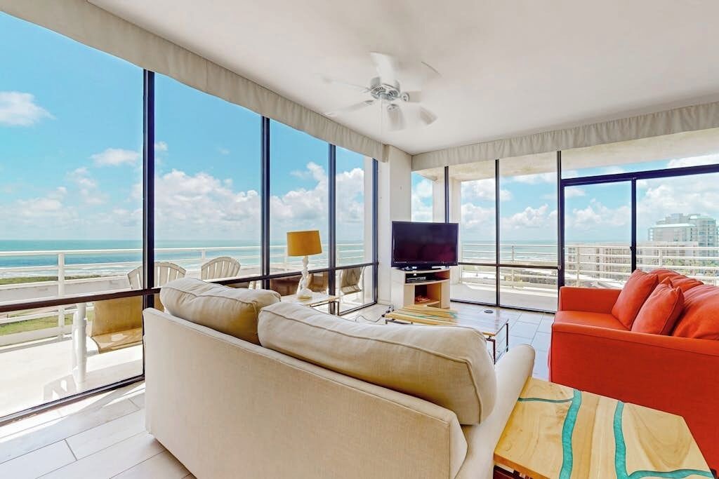A modern living room with a large window, a ceiling fan, a flat-screen TV, and a red sofa.