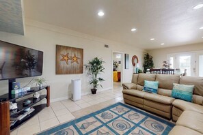 A living room with a television, a starfish wall art, a beige sofa, and a patterned rug. - Butterfly Vine Escape Beach House (South Padre Island)