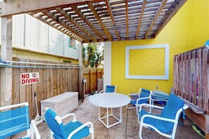 Eine Außenpatio mit einer Holz-Pergola, einem weißen Tisch, blauen Stühlen und einem Schild mit der Aufschrift 'NO DIVING'.