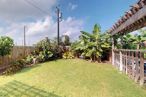 Ein Garten mit Holzzaun, einer Pergola und verschiedenen Pflanzen, darunter Bananenbäume.