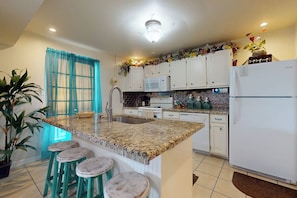 A kitchen with a granite countertop, white cabinets, a white refrigerator, and a sink. There are three stools at the counter. - Butterfly Vine Escape Beach House (South Padre Island)