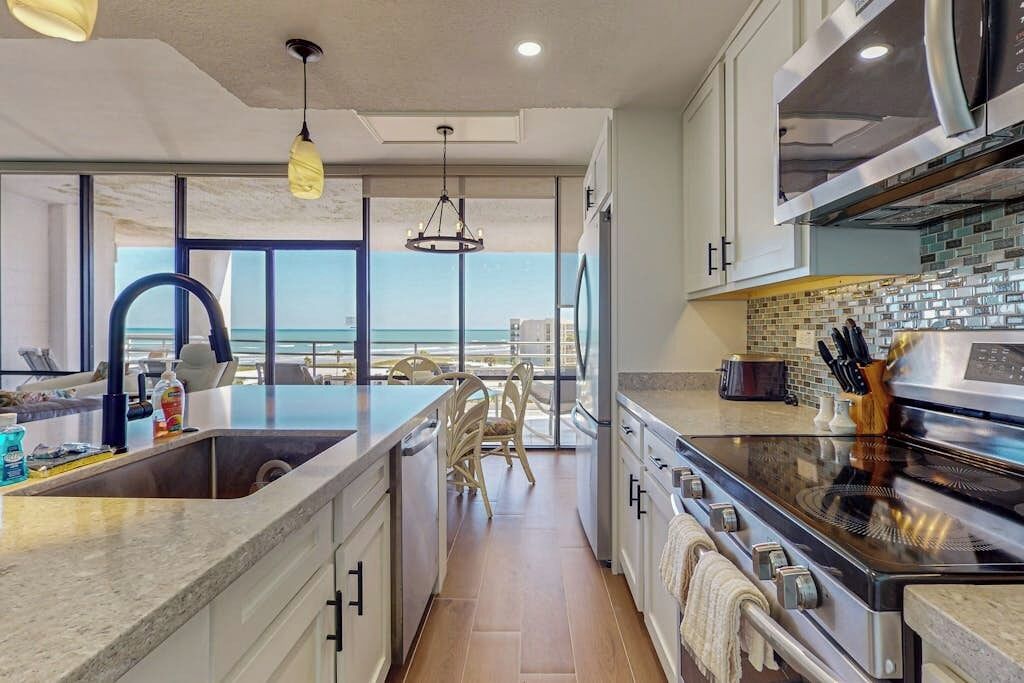 A modern kitchen with a large island, stainless steel appliances, and a view of the ocean.