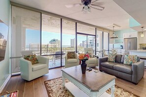 A spacious living area with a large window, a ceiling fan, and a modern kitchen in the background. - Sunchase IV #515 - Gulf & Bay Views, Hot Tub (South Padre Island)