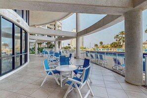 Un espace extérieur aménagé avec des meubles de jardin bleus, comprenant des chaises et des tables, et abrité par un auvent, d’où l’on peut admirer une piscine et le paysage urbain.