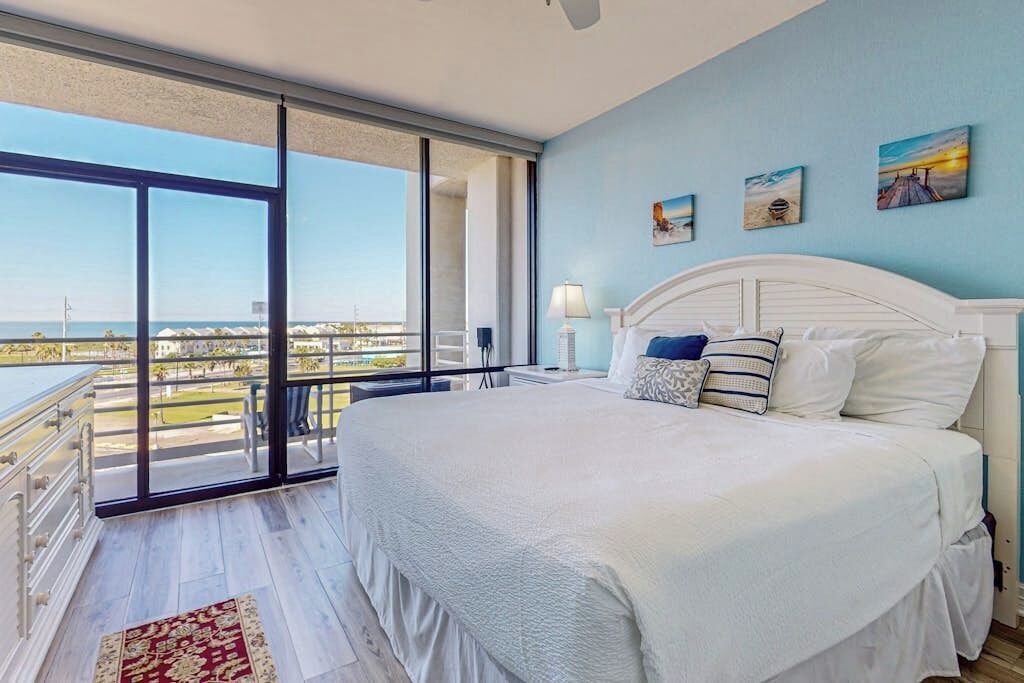 A bedroom with a large bed, a view of the city, and a balcony.