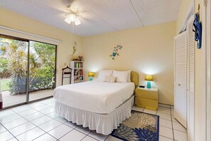 A bedroom with a bed, bedside tables, a bookshelf, and a sliding glass door to a garden. - Ventura Condominiums #101 (South Padre Island)