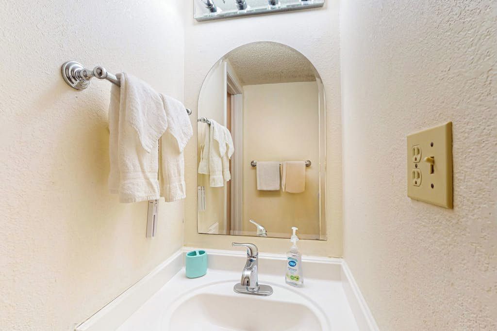 Un baño con un lavabo blanco, un espejo y un perchero con varias toallas.