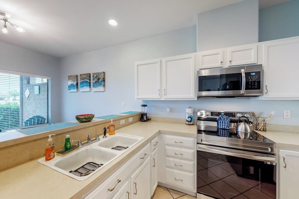 A modern kitchen with white cabinets, a stainless steel microwave, an oven, and a sink with a dish rack.