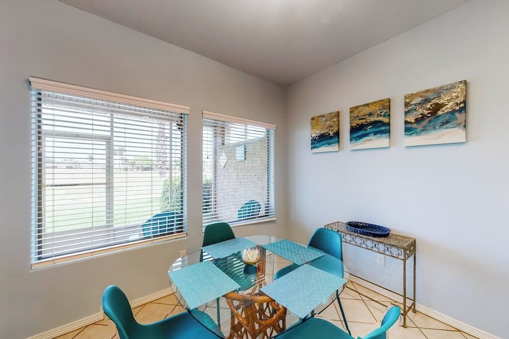A dining area with a glass table, blue chairs, and a metal side table with a blue bowl.
