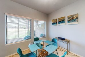 A dining area with a glass table, blue chairs, and a metal side table with a blue bowl. - Serene Sanctuary at 20 Torrey Pines (Laguna Vista)