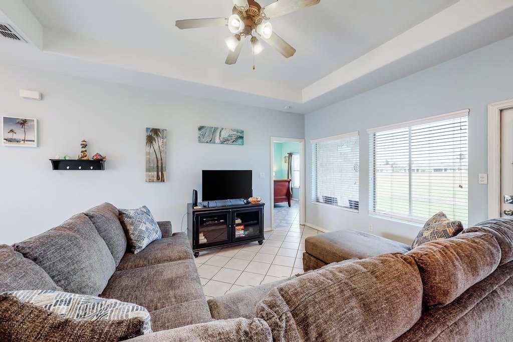 A living room with a large sectional sofa, a flat-screen TV on a black stand, and a ceiling fan.