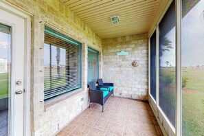 A covered patio area with a stone wall, a wicker chair, and a door leading outside. - Serene Sanctuary at 20 Torrey Pines (Laguna Vista)