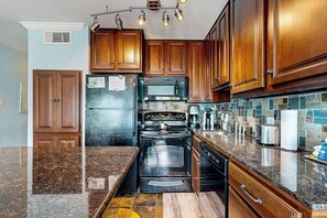 Eine Küche mit Holzausstattung, einem Edelstahl-Kühlschrank, einer Mikrowelle, einem Backofen und einer Arbeitsplatte aus Granit.