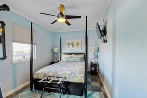 Ein Bett mit Baldachin, ein Deckenventilator, ein Fenster mit Jalousien und ein an der Wand befestigter Fernseher.