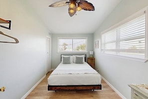 A bedroom with a bed, a ceiling fan, a window with blinds, and a nightstand. - The Anchor Inn - Big Balcony, Steps to the Beach (Galveston)