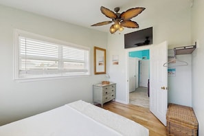 A bedroom with a bed, a dresser, a ceiling fan, a window with blinds, and a door leading to another room. - The Anchor Inn - Big Balcony, Steps to the Beach (Galveston)