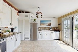 A spacious kitchen with white cabinets, a stainless steel refrigerator, and a large window. - The Anchor Inn - Big Balcony, Steps to the Beach (Galveston)