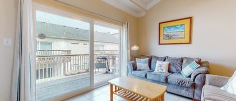 A living room with a sofa, a coffee table, and a sliding glass door leading to an outdoor area with a barbecue.