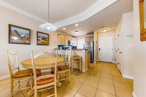 A kitchen with a dining area, featuring a central island, white cabinetry, and a hanging light fixture. - Rain Dancer Condominiums 10 (South Padre Island)
