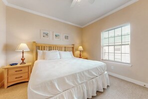 A bedroom with a bed, two bedside tables, a window with blinds, and three framed pictures on the wall. - Rain Dancer Condominiums 10 (South Padre Island)
