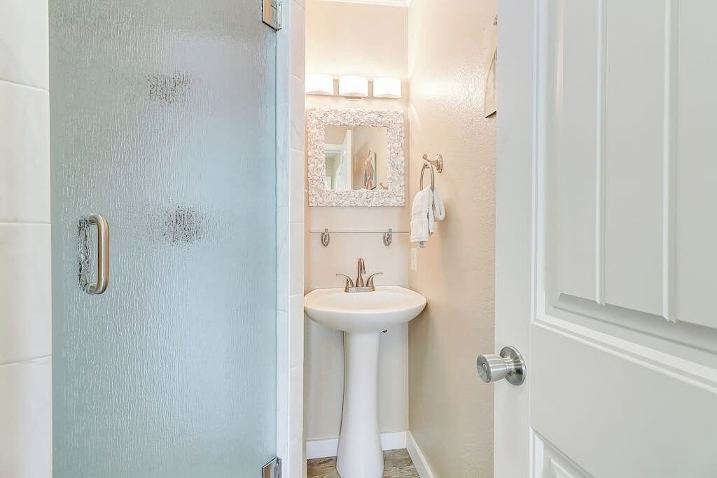 Un baño con un lavamanos pedestal blanco, un espejo con marco decorativo y un perchero.
